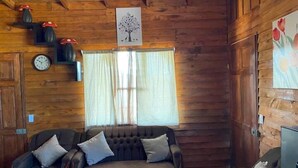 A cozy cabin interior with a wooden ceiling, a large window with curtains, a wall clock, and a framed picture of a tree. - Red Princess Cabin - PERFECT view of the valley! (San José)