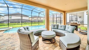 A covered patio area with wicker furniture, a pool, and a barbecue grill. - Spacious 10-Bedroom Family Retreat Near Disney (Kissimmee)