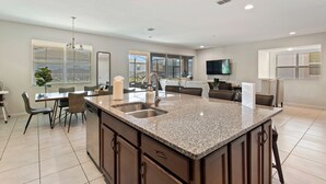 A spacious kitchen with granite countertops, a central island with a sink, and dark wooden cabinets. - Spacious 10-Bedroom Family Retreat Near Disney (Kissimmee)