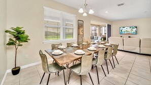 A dining area with a table set for six, a potted plant, and a television mounted on the wall. - Spacious 10-Bedroom Family Retreat Near Disney (Kissimmee)