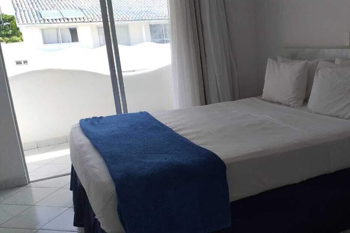 A hotel room with a bed, a nightstand, and a view of the outside.