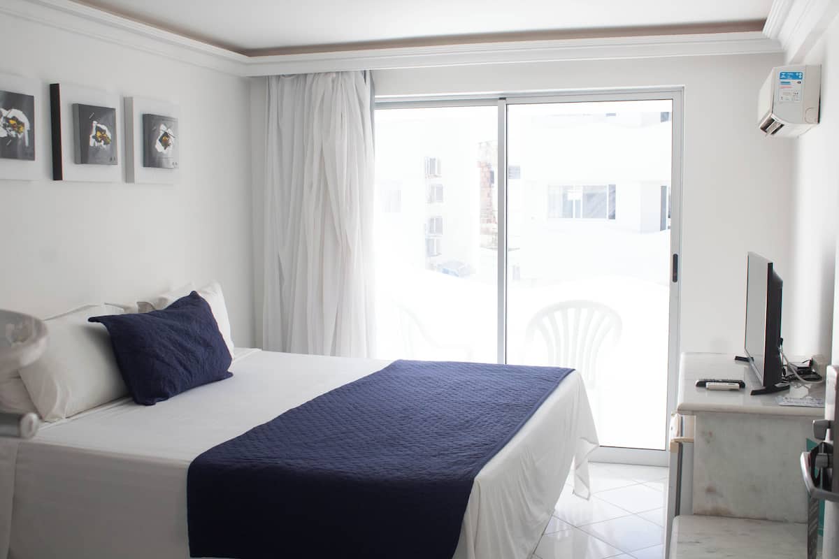A hotel room with a bed, a desk with a computer, and a window with a view of buildings.