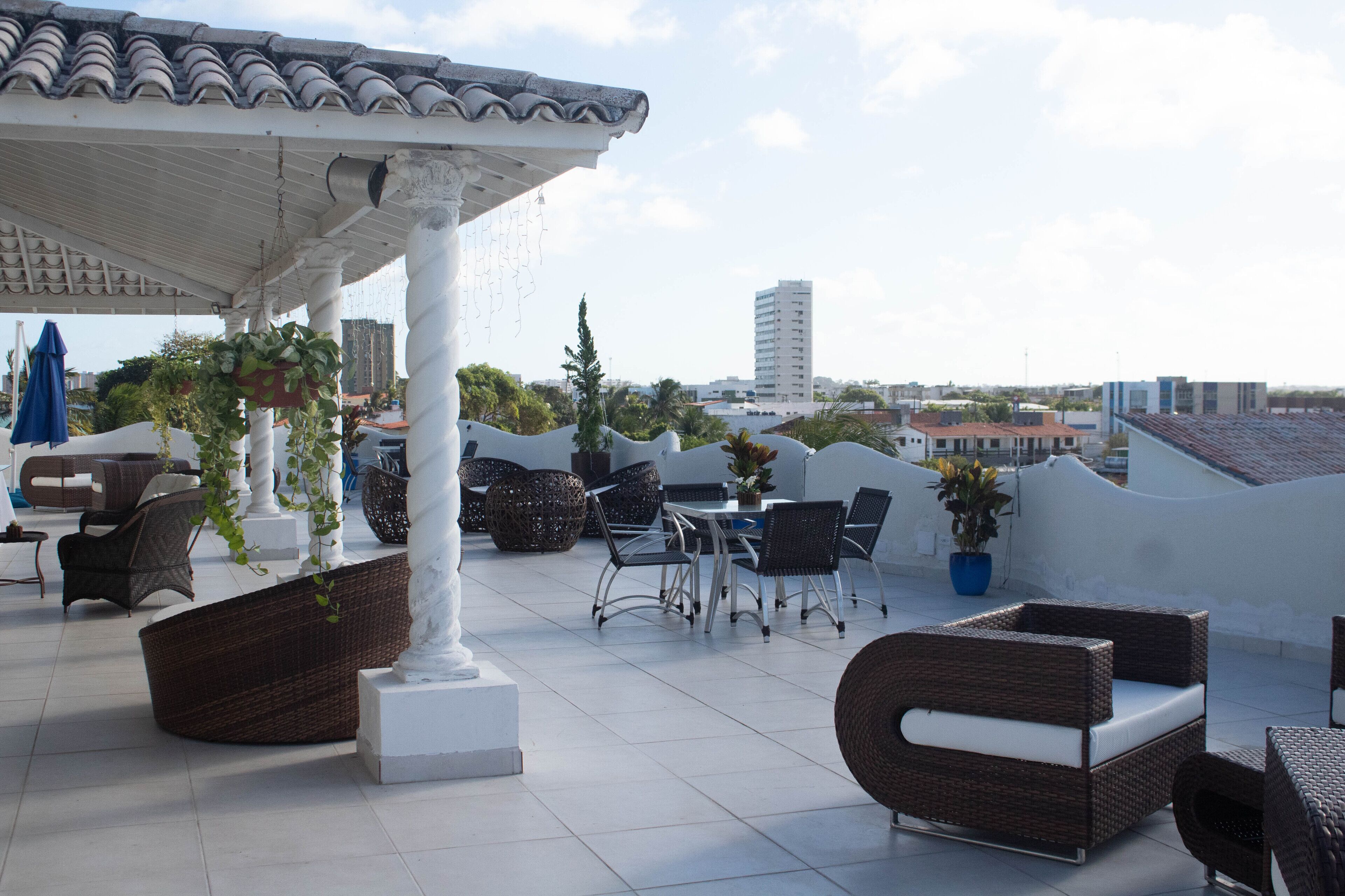 A rooftop terrace with wicker furniture, potted plants, and a view of the cityscape.