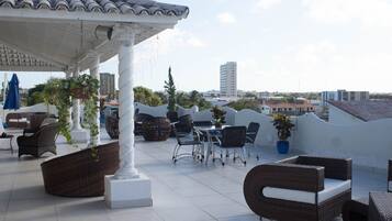 A rooftop terrace with wicker furniture, potted plants, and a view of the cityscape.