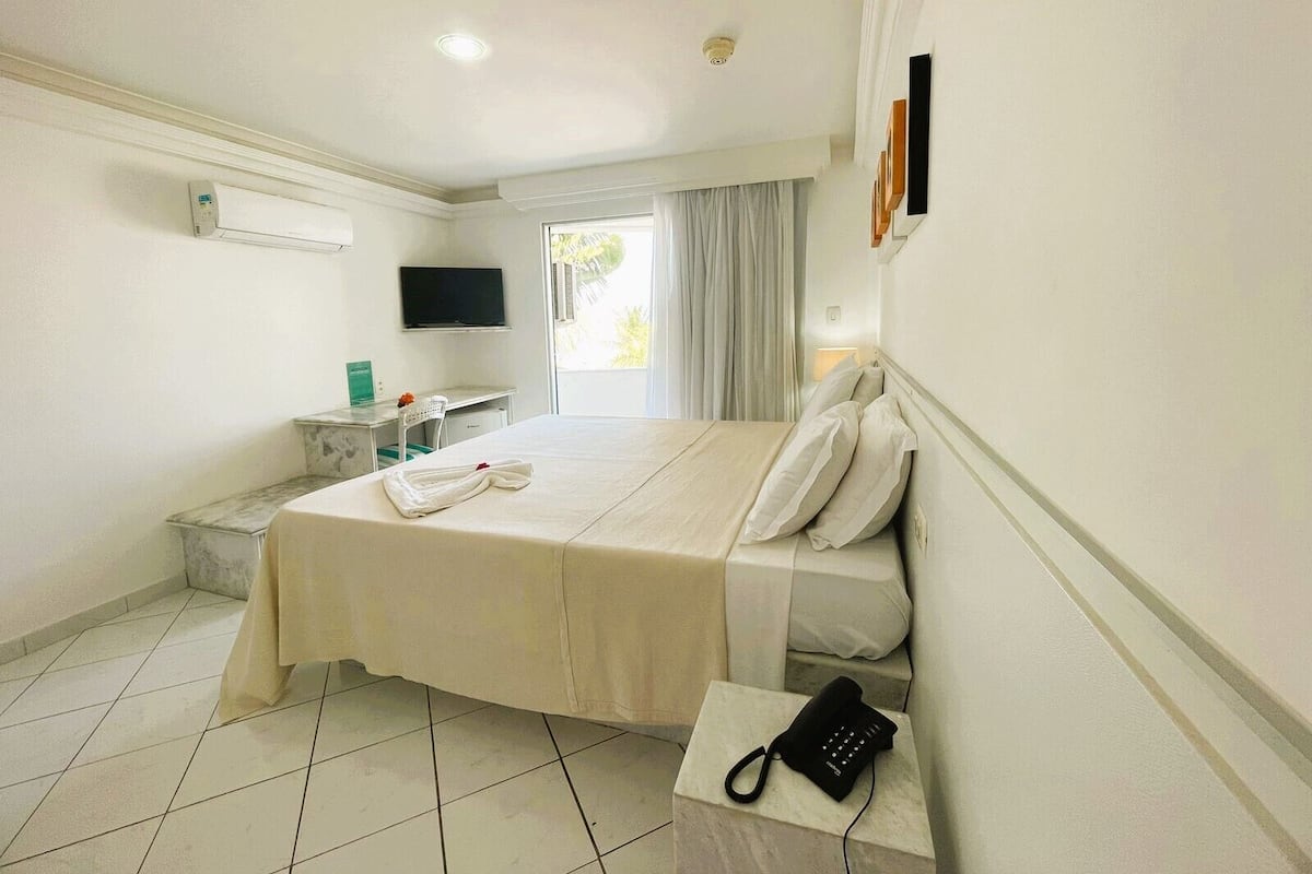 A hotel room with a bed, a desk, a TV, a phone, and a window with curtains.