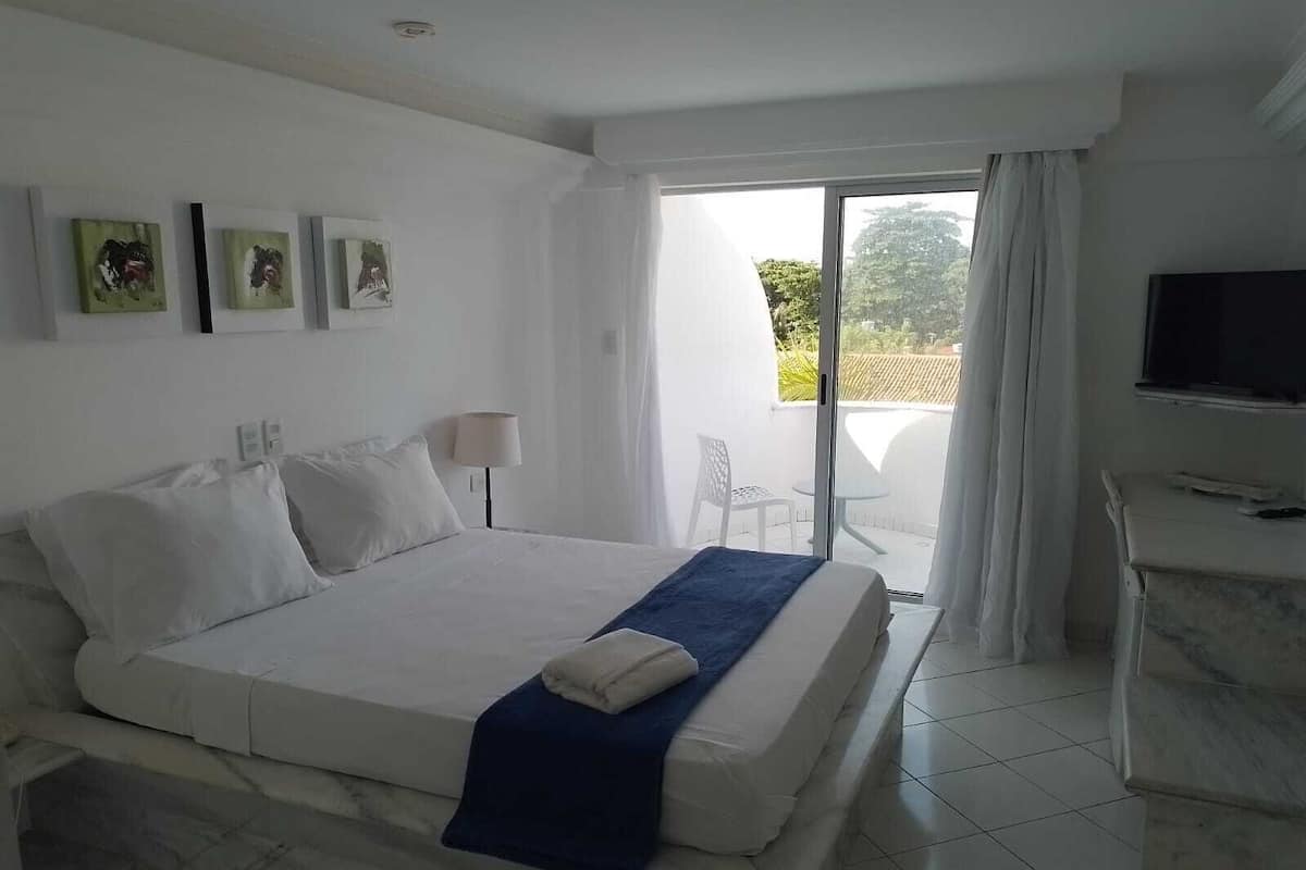 A hotel room with a bed, a TV, a balcony with a chair, and artwork on the wall.