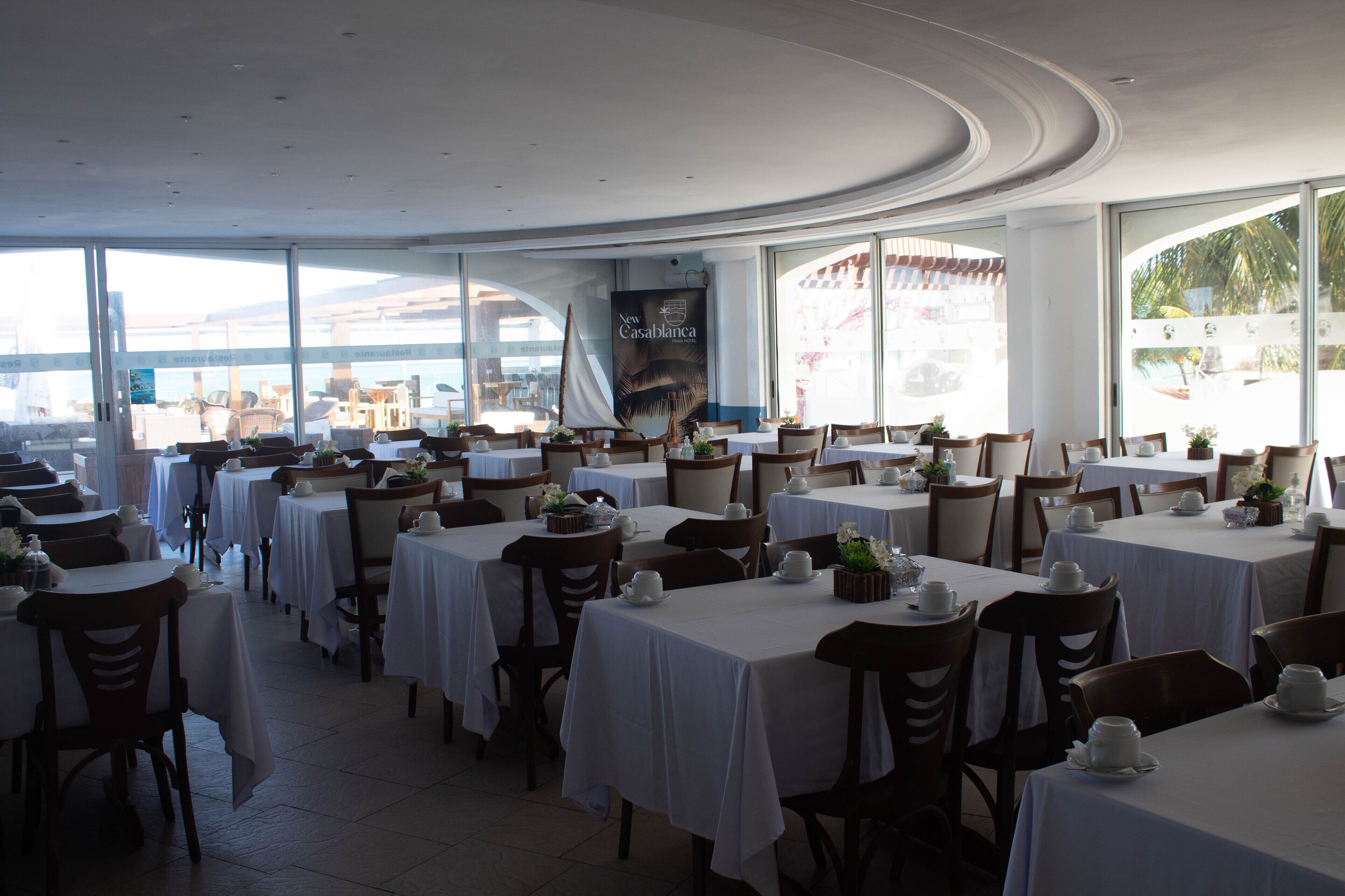 Un restaurant amb diverses taules i cadires, grans finestres i vista cap a l'exterior.