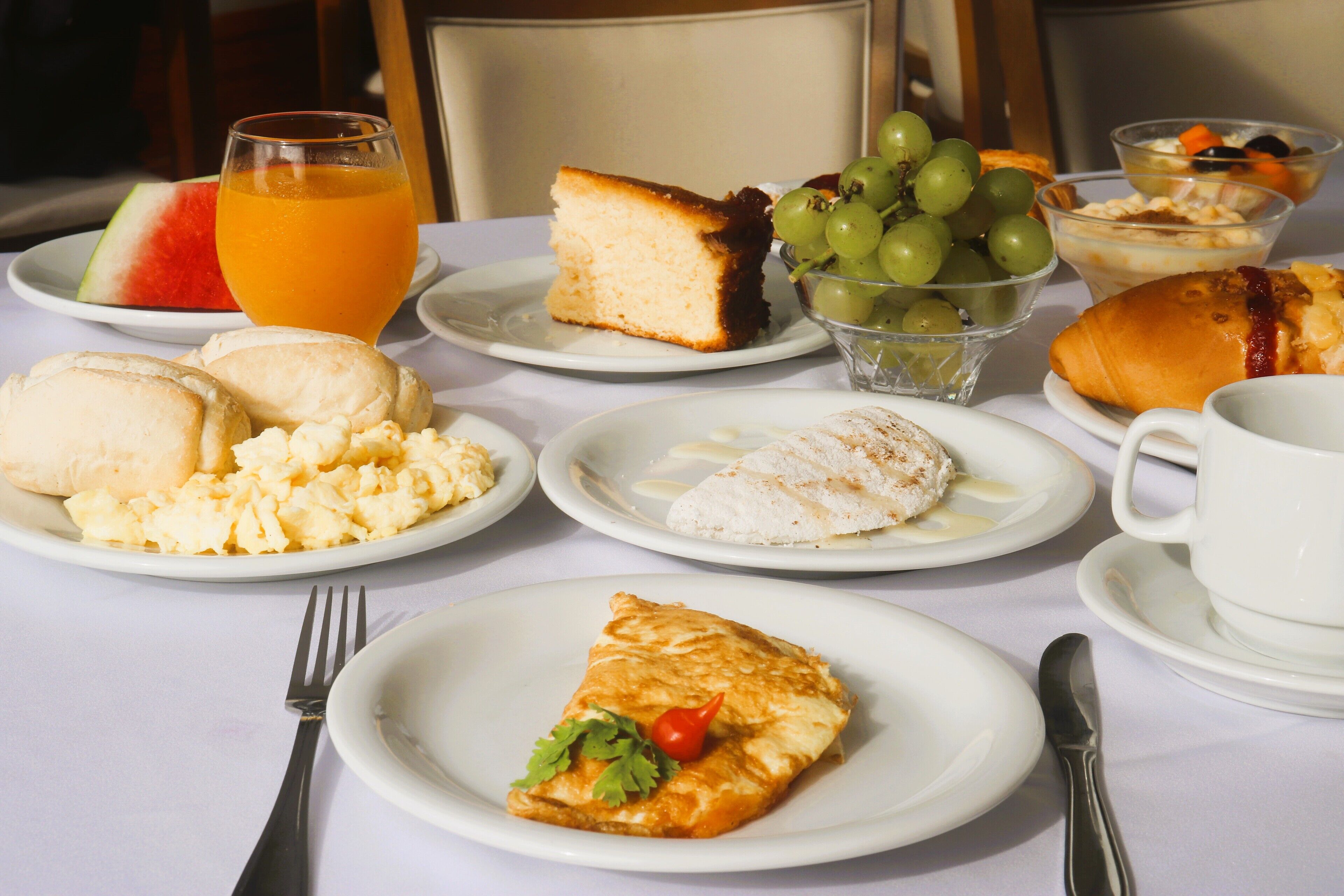 Ein Frühstückstisch mit verschiedenen Speisen, darunter Eier, Toast, ein Stück Kuchen und ein Glas Orangensaft.