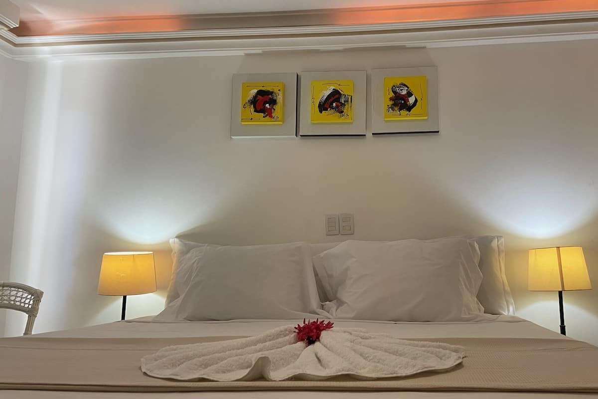 A hotel room with a bed, two bedside lamps, and three framed artworks on the wall.