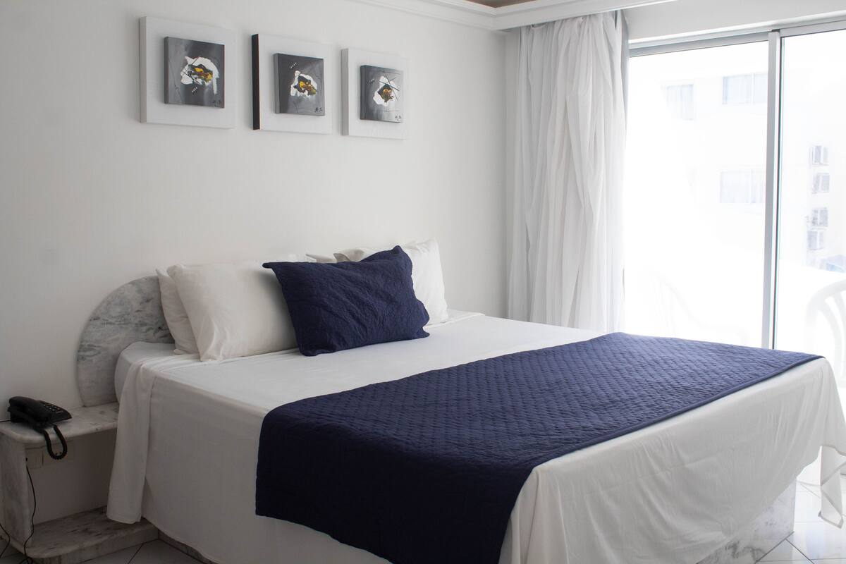 A hotel room with a large bed, a nightstand with a phone, and three framed artworks on the wall.