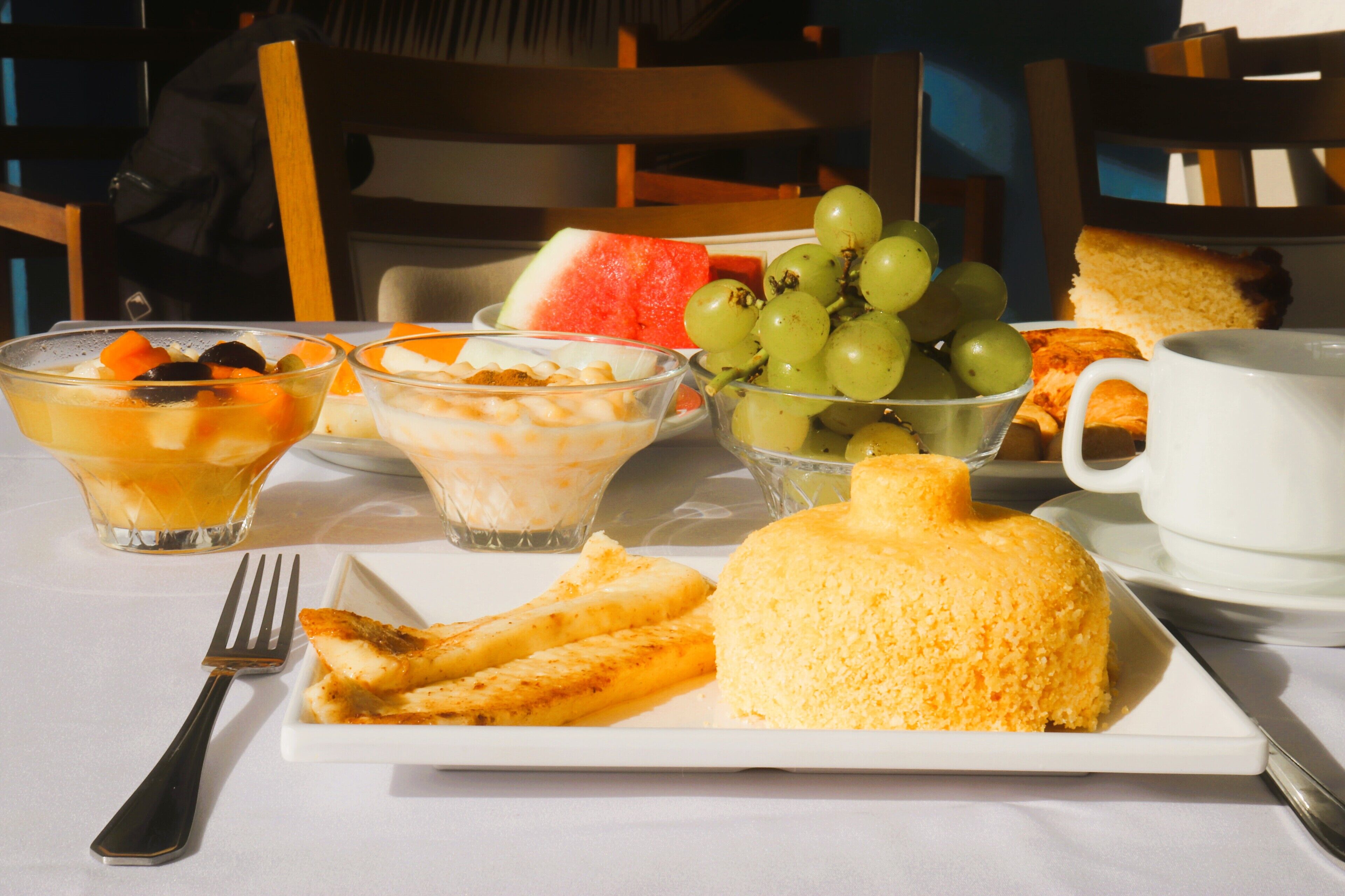 A breakfast setting with a plate of food, bowls of fruit, and a cup of coffee on a table.