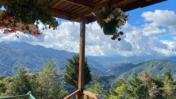 Eine hölzerne Pergola mit blühenden Ampeln vor einer Berglandschaft.