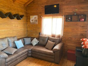 A cozy cabin interior with a brown leather sofa, a flat-screen TV mounted on the wall, and a window with curtains.