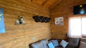 Ein gemütliches Blockhaus mit Holzwänden, einem braunen Ledersofa, einem Flachbildfernseher und einem Fenster mit Vorhängen.
