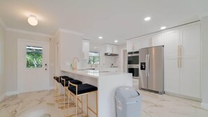A modern kitchen with white cabinets, a stainless steel refrigerator, and a marble floor. - The Villa #1 (North Palm Beach)