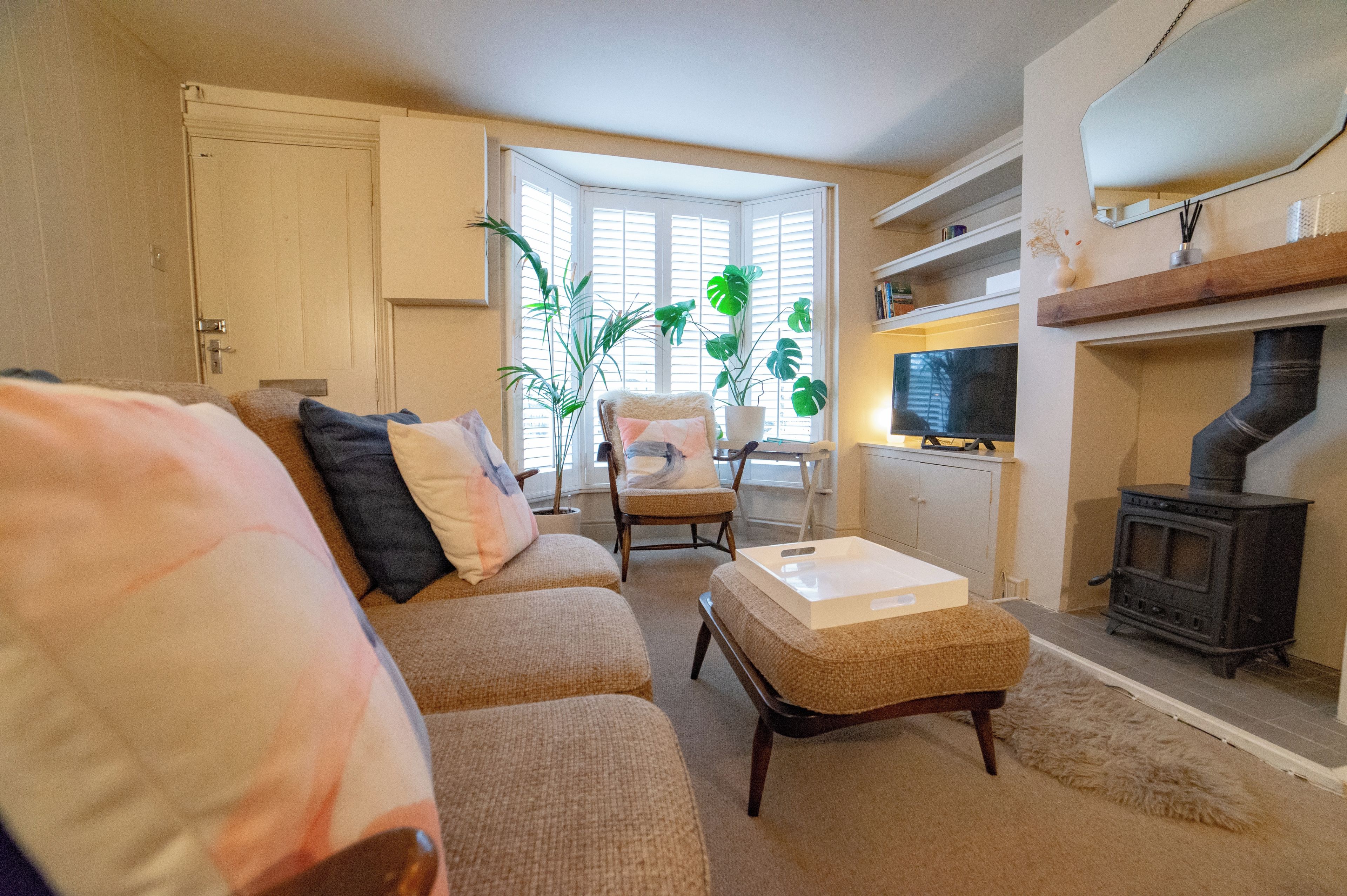 A living room with a sofa, armchair, ottoman, and a television. There is a fireplace and a window with blinds.