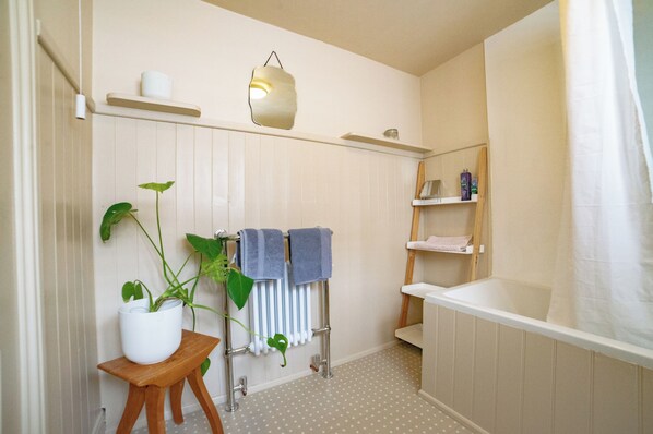 A bathroom with a bathtub, a shower, a toilet, a sink, a mirror, a towel rack, a potted plant, and a shelf with toiletries.