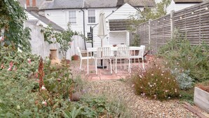 Un patio ajardinado con mobiliario exterior blanco, rodeado de diversas plantas y flores.