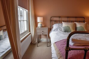 Une chambre à coucher avec un lit, une table de chevet, une lampe et une fenêtre avec des rideaux.