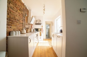A kitchen with white cabinets, a brick wall, and a wooden floor.