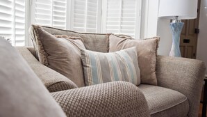 Ein Wohnzimmer mit einer Couch, Kissen, einer Lampe und einem Fenster mit Jalousien.