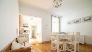 Ein helles Wohnzimmer mit Holzboden, einer Couch, einem Esstisch mit Stühlen und einer Kristallleuchter.