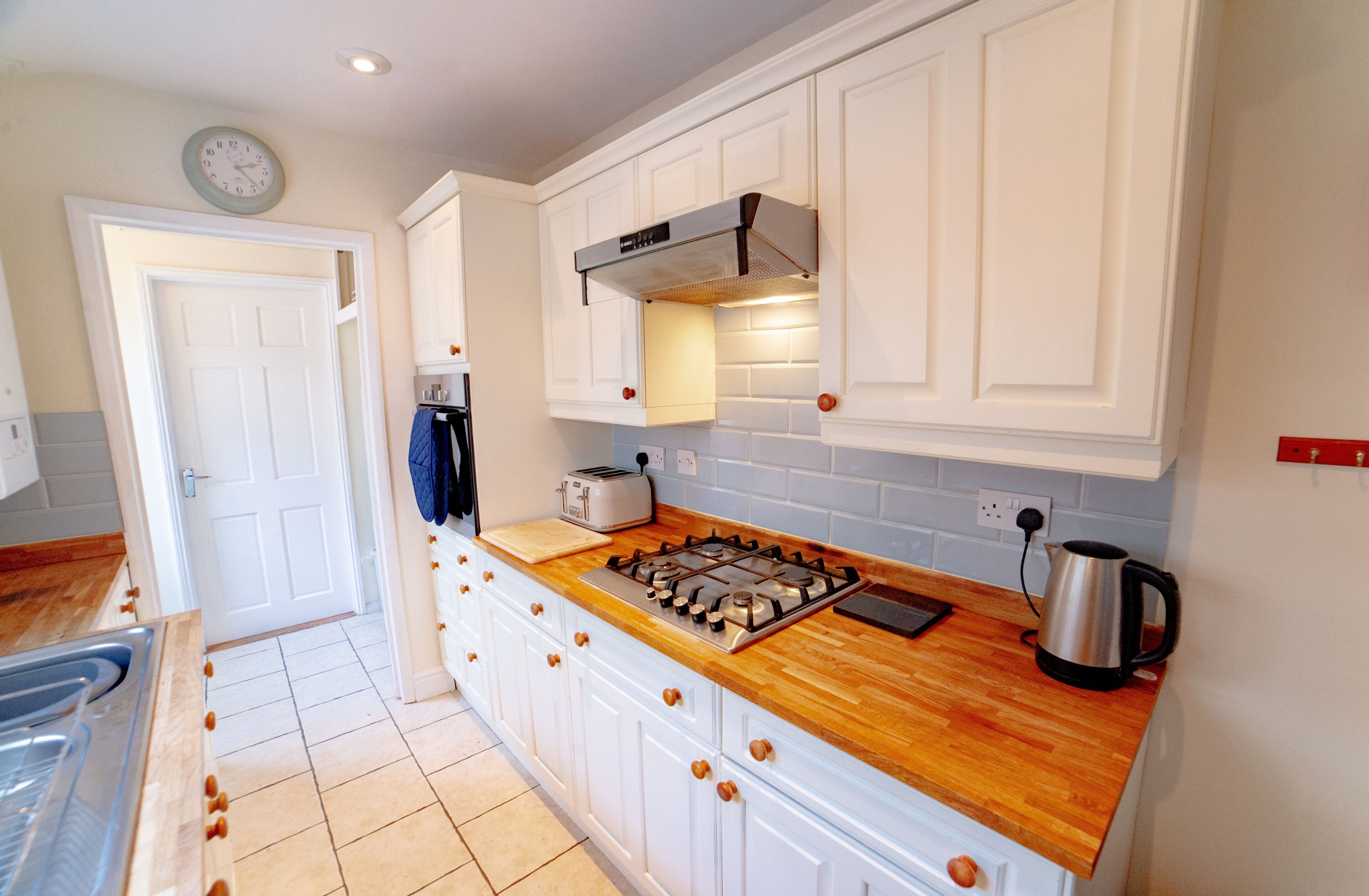 A kitchen with white cabinets, a wooden countertop, a gas stove, a toaster, and a kettle.