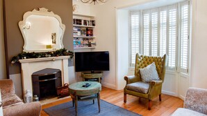 A living room with a fireplace, television, bookshelf, and a large window with shutters. - Harbour House is a lovingly refurbished and centrally located beautiful three storey house, sleeping 9 guests, with private parking. (Whitstable)