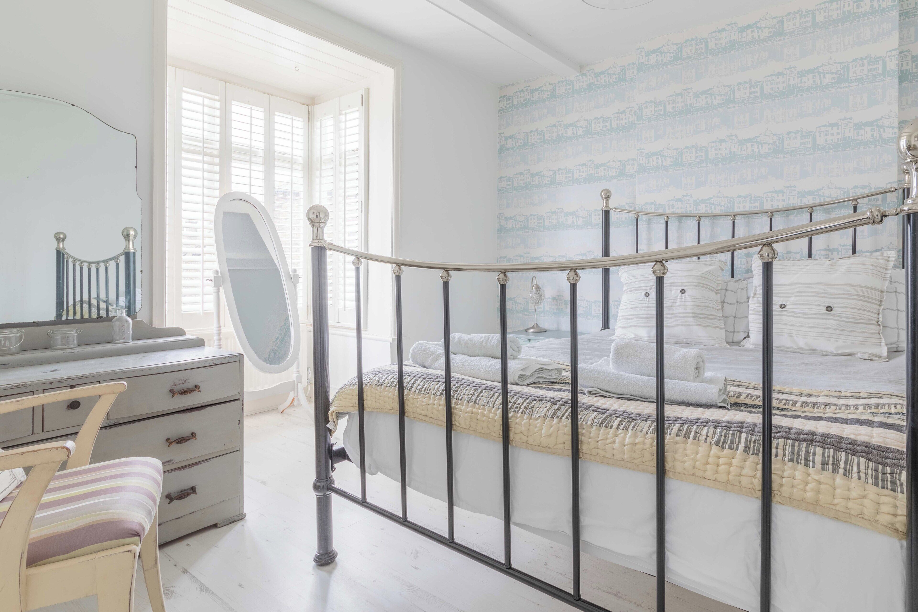 Ein Schlafzimmer mit einem Bett, einem Schminktisch, einem Sessel und einem Fenster.