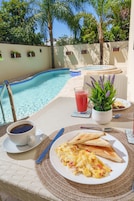Desayuno junto a la piscina con una bebida, tostadas y huevos revueltos sobre una mesa.