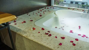 A bathtub with rose petals on the floor, a wooden bench, and a view of buildings outside. - La Casona MC (La Romana)
