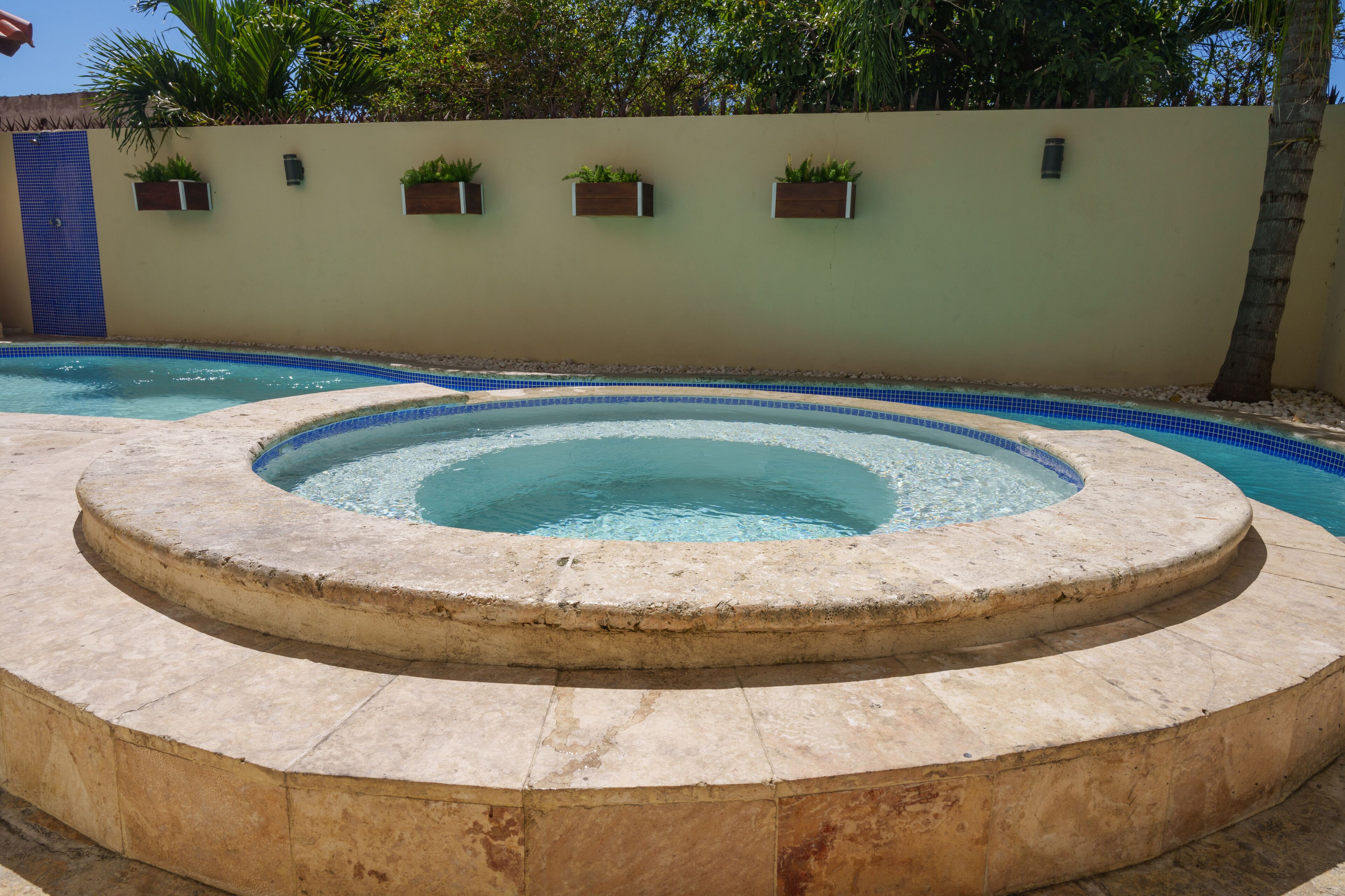 Una piscina con un jacuzzi en el centro, rodeada por una terraza de piedra.