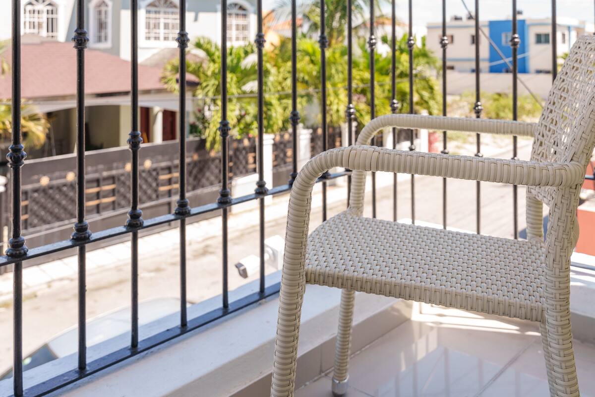 A balcony with a wicker chair, a metal railing, and a view of buildings and palm trees.