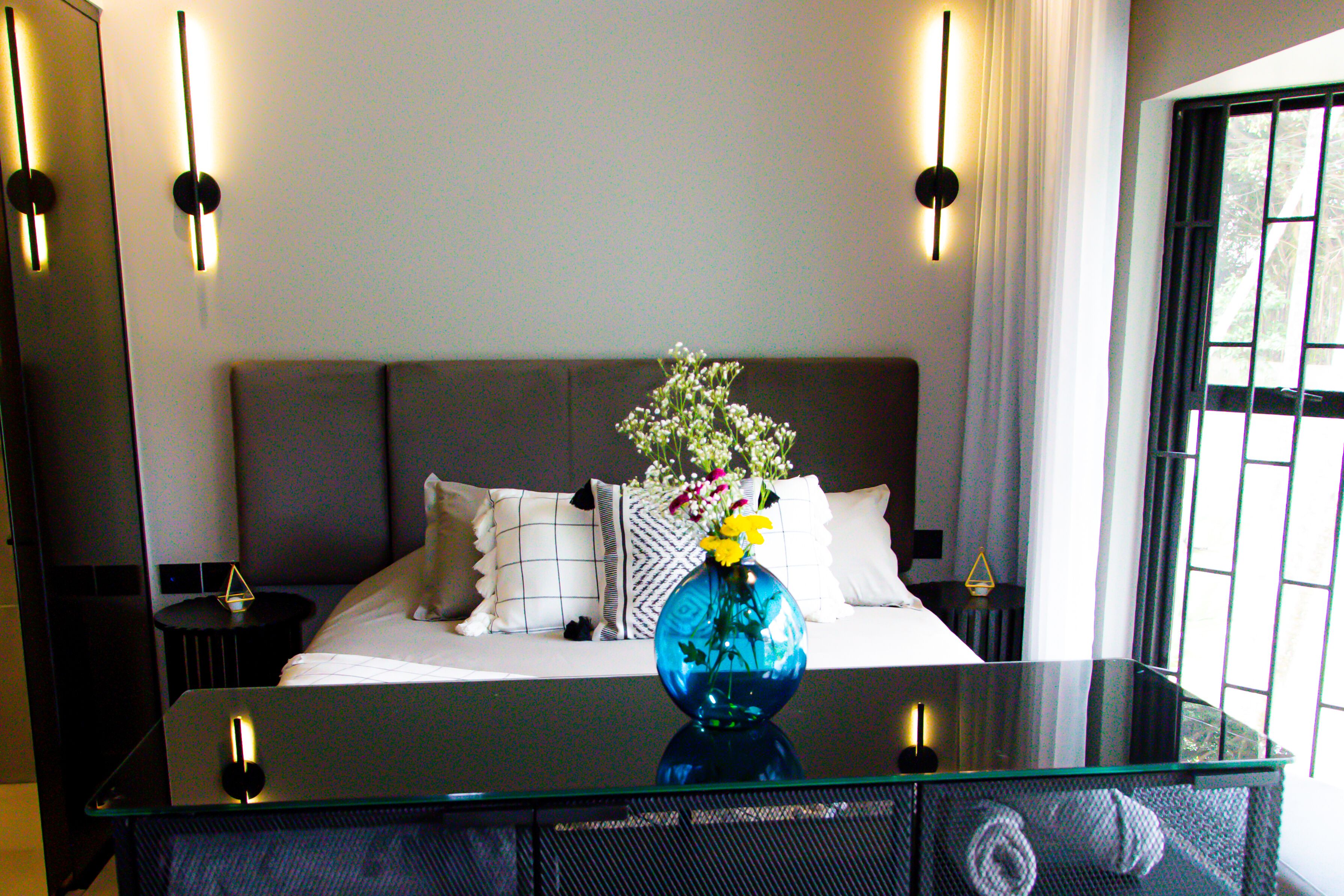 A modern hotel room with a large bed, a glass coffee table, and a vase with flowers.
