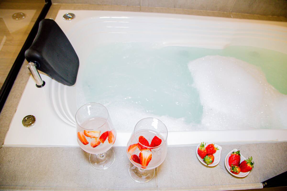A bathtub with two glasses of water containing strawberries, and a small plate with strawberries.
