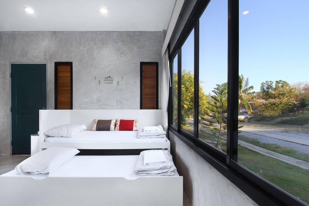 A modern bedroom with two beds, a large window, and a wall with a mountain and trees design.