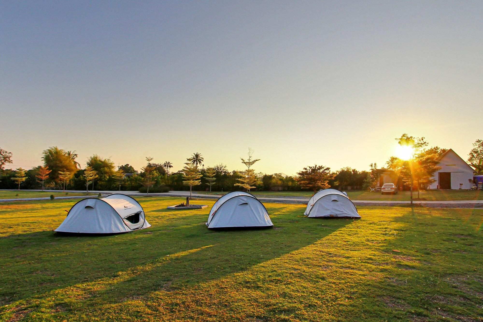 Three tents on a grassy field with a barn and trees in the background.