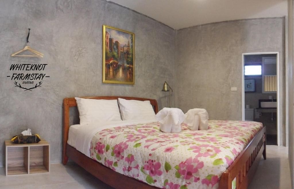 Un dormitorio con cama, mesita de noche, un cuadro y una puerta que da a otra habitación.