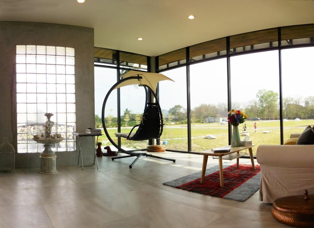 A spacious room with large windows, a hanging chair, a small table with a vase, and a white sofa.