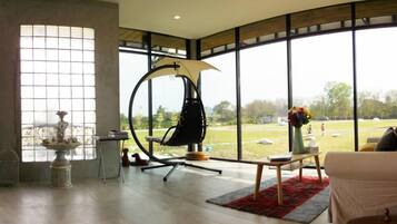 A spacious room with large windows, a hanging chair, a small table with a vase, and a white sofa.