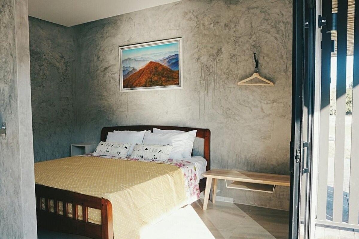 A bedroom with a bed, a wooden bench, a hanging light fixture, and a framed picture on the wall.