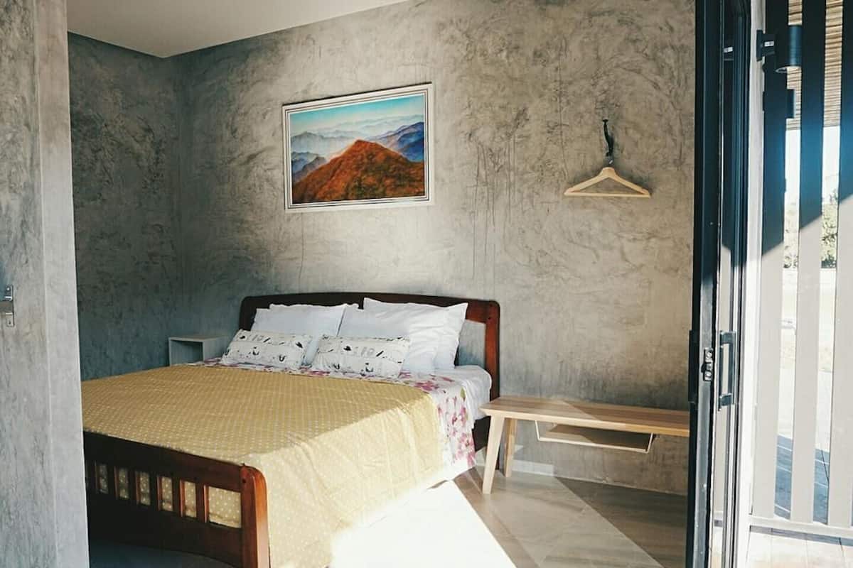 A bedroom with a bed, a wooden bench, a hanging light fixture, and a framed picture on the wall.