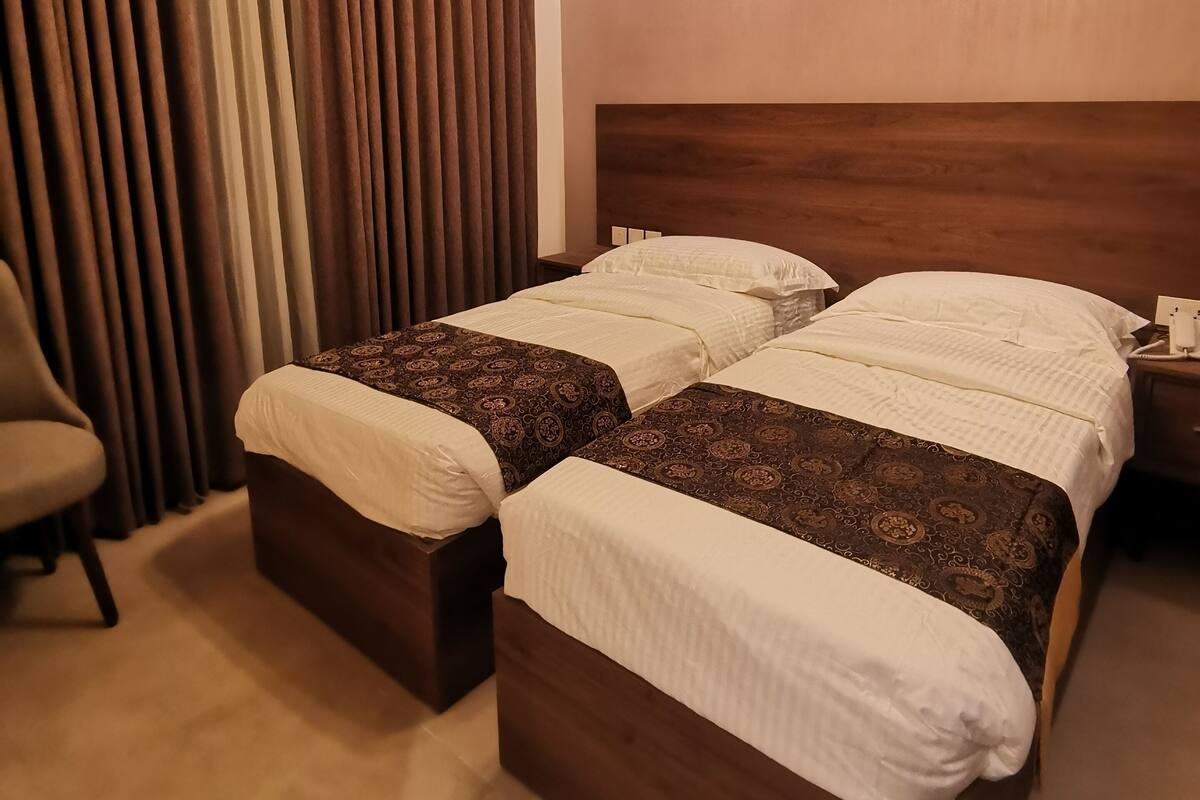 A hotel room with two beds, a chair, a nightstand, and a ceiling light fixture.