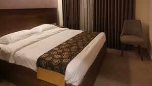 A hotel room with a wooden headboard, a large bed with white and patterned bedding, a chair, and a ceiling light fixture. - Dara apartment hotel (Amman)