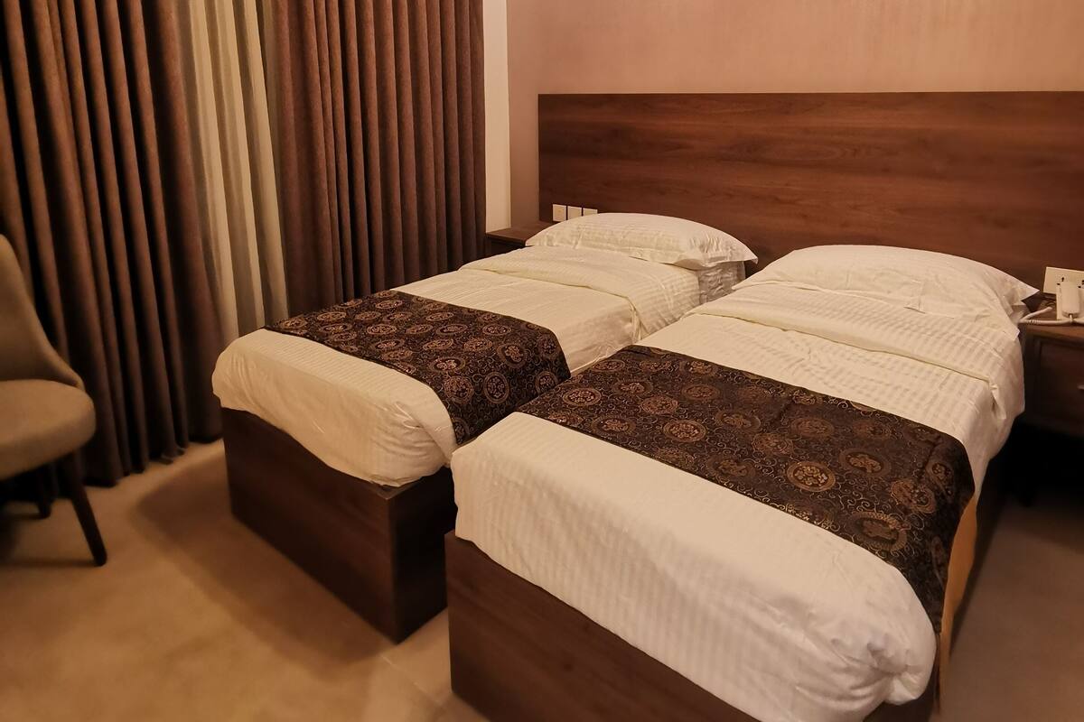 A hotel room with two beds, a chair, a nightstand, and a modern chandelier.