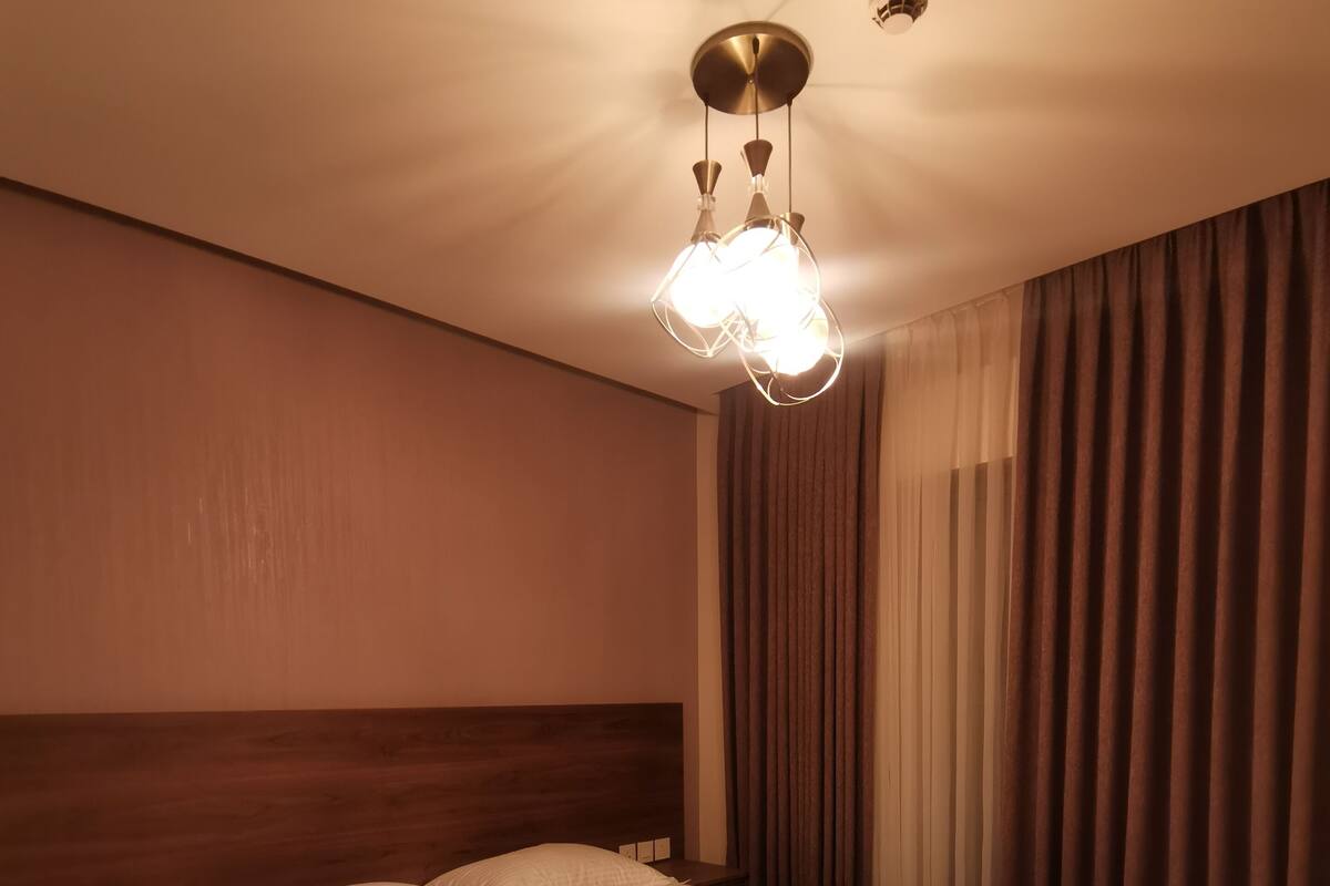 A hotel room with a large bed, a nightstand, a telephone, and a ceiling light fixture.