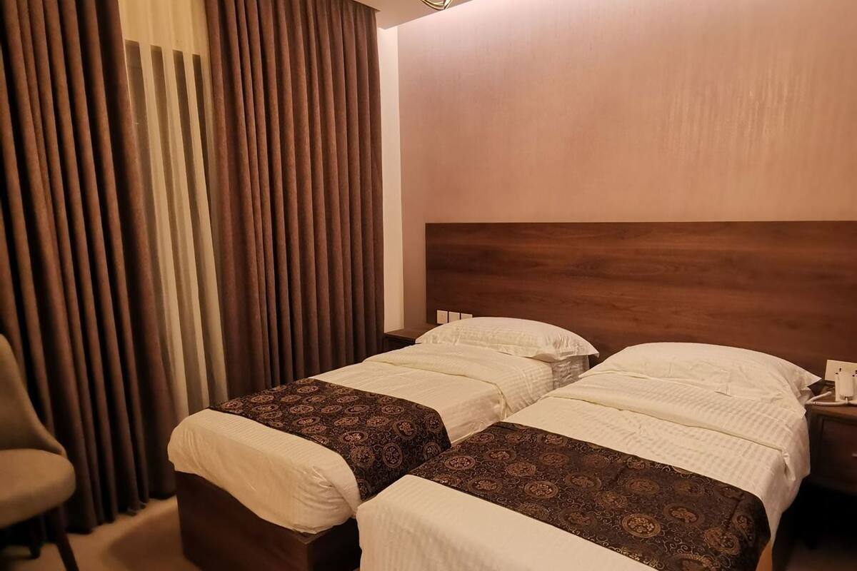 A hotel room with two beds, a chair, a nightstand, and a ceiling light fixture.
