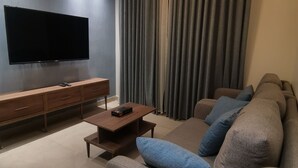 A modern living room with a flat-screen TV, a wooden coffee table, a sofa with blue cushions, and a large window with curtains. - Dara apartment hotel (Amman)