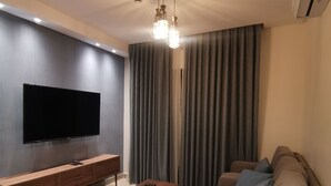 A modern living room with a flat-screen TV, wooden entertainment unit, and a sofa with blue cushions. - Dara apartment hotel (Amman)