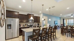 A modern kitchen with dark wood cabinets, stainless steel appliances, and a central island with bar stools. - Amazing 6Bd W/ GameRoom & Pool (Kissimmee)